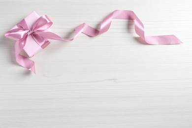 Beautiful gift box with pink bow on white wooden background, top view. Space for text