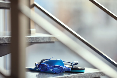 Photo of Swimming cap, goggles and flip flops on stairs indoors
