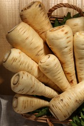 Wicker basket with delicious fresh ripe parsnips and green leaves on wooden table, top view