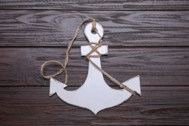 Photo of White anchor with hemp rope on dark wooden table, top view
