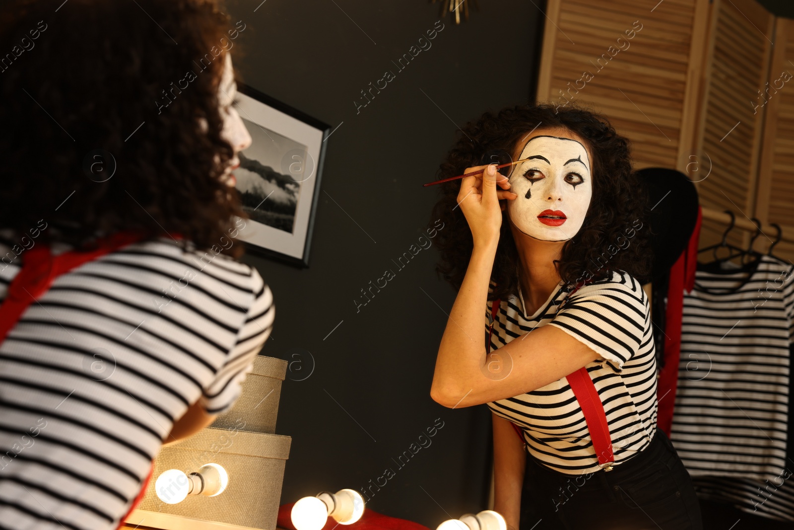 Photo of Young woman applying mime makeup near mirror indoors