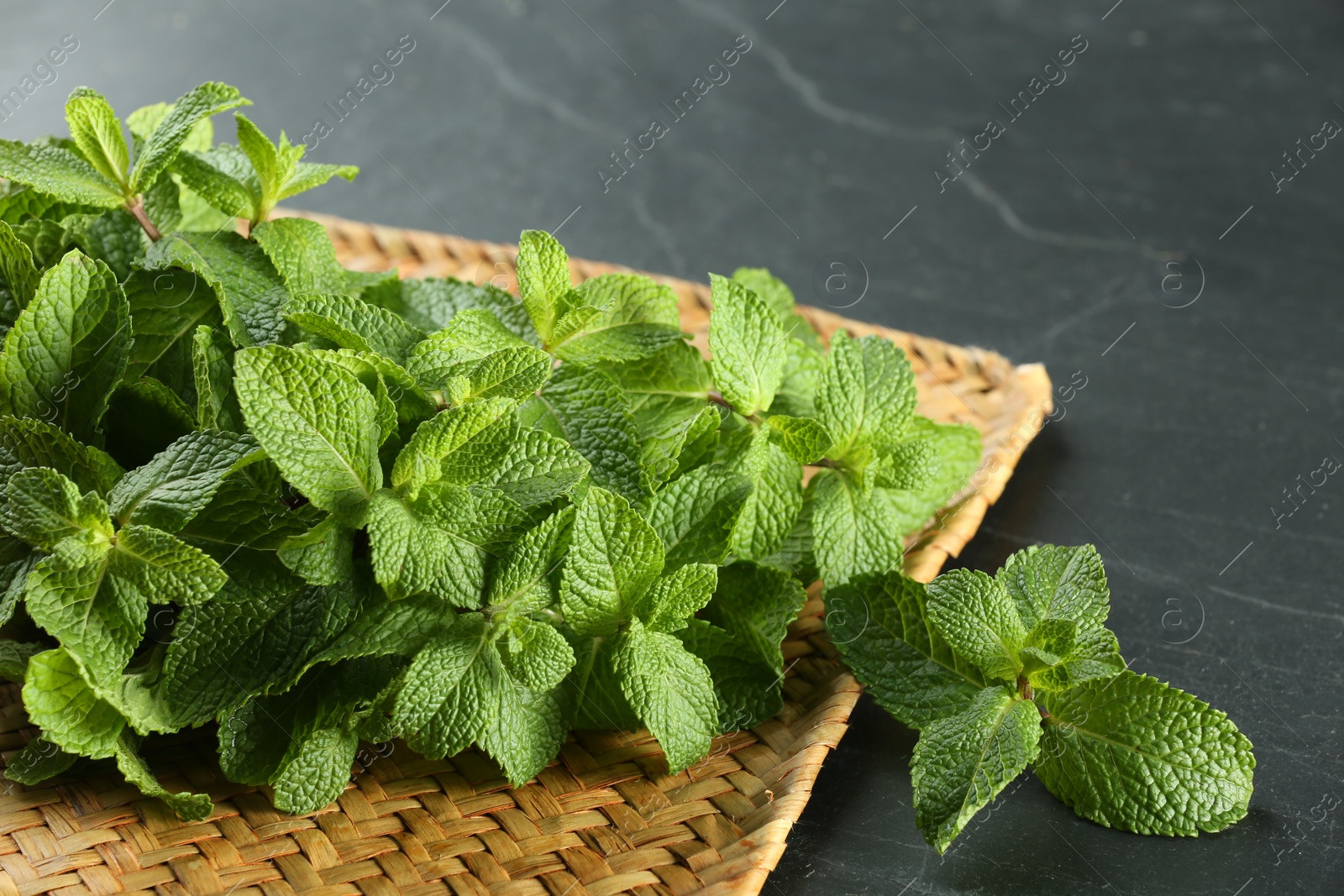 Photo of Wicker mat with fresh green mint leaves on black table, closeup