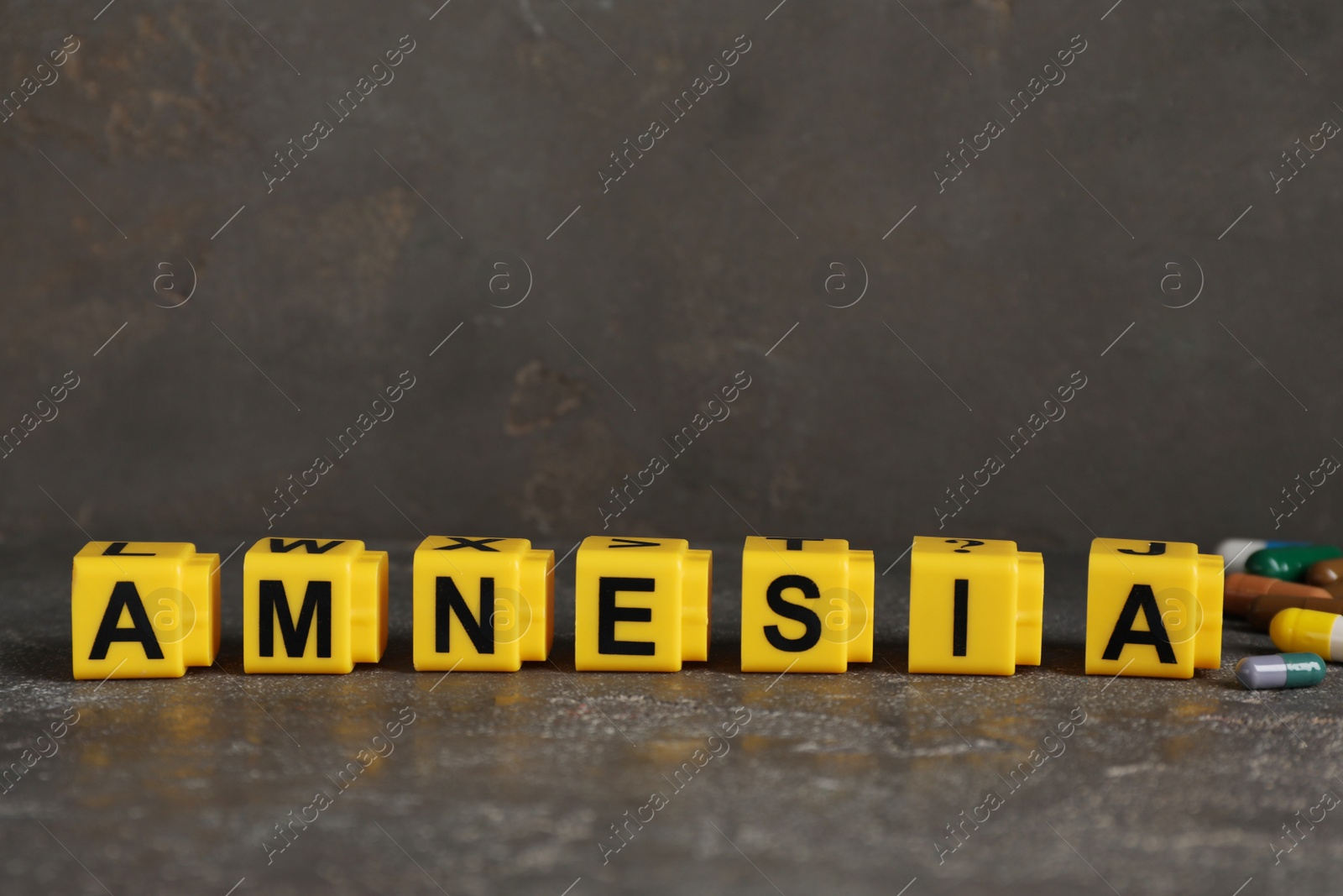 Photo of Yellow cubes with word Amnesia and pills on grey table, closeup