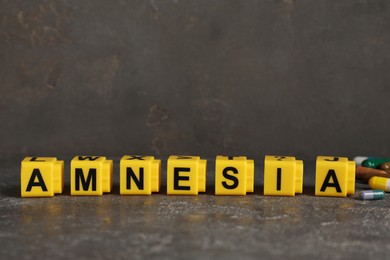 Yellow cubes with word Amnesia and pills on grey table, closeup