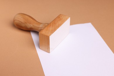 One wooden stamp tool and sheet of paper on light brown background, closeup. Space for text