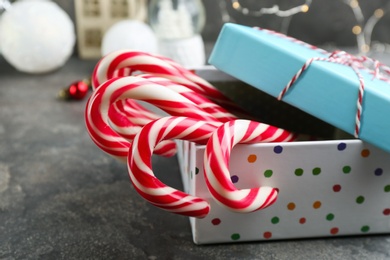 Photo of Many sweet candy canes in gift box on grey table, closeup. Traditional Christmas treat
