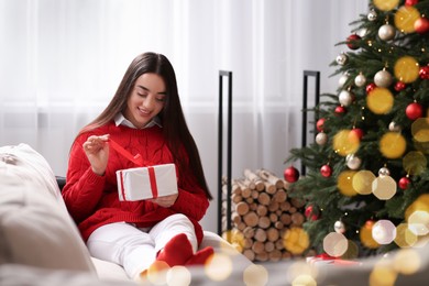 Smiling woman opening gift near Christmas tree indoors