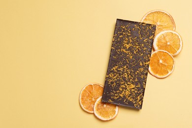 Photo of Chocolate bar with freeze dried orange on yellow background, flat lay. Space for text