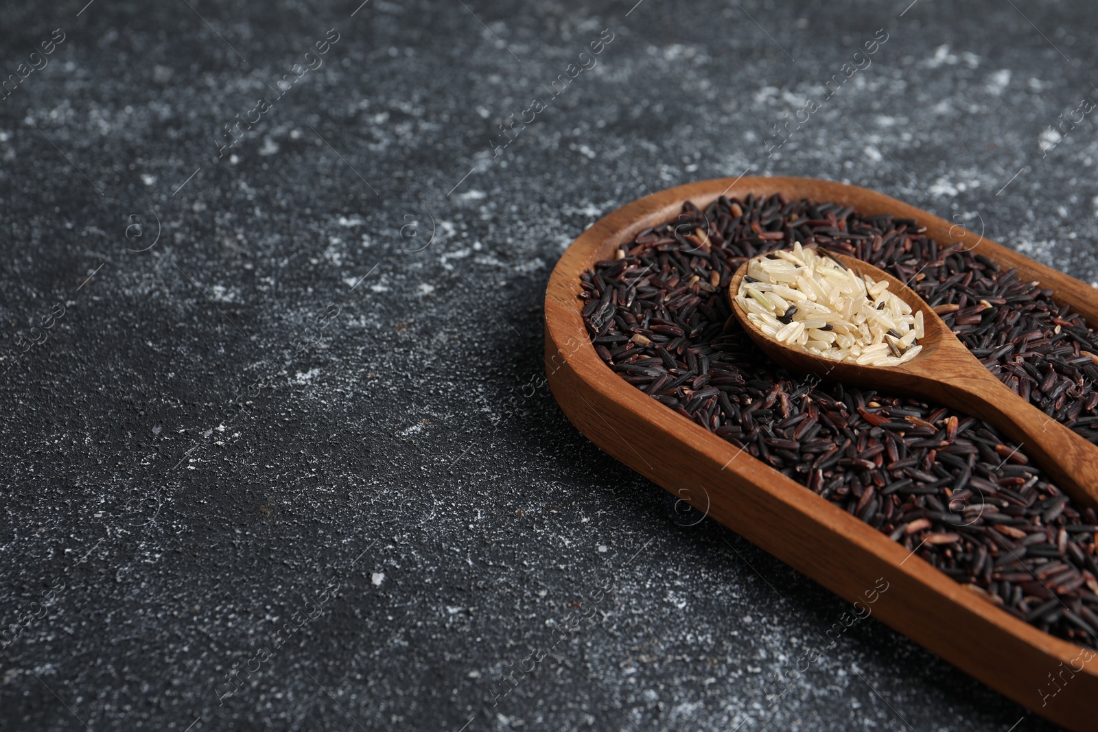 Photo of Spoon and dish with different sorts of rice on black textured table. Space for text