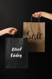 Photo of People holding paper bags with phrases Black Friday and Sale against dark background, closeup