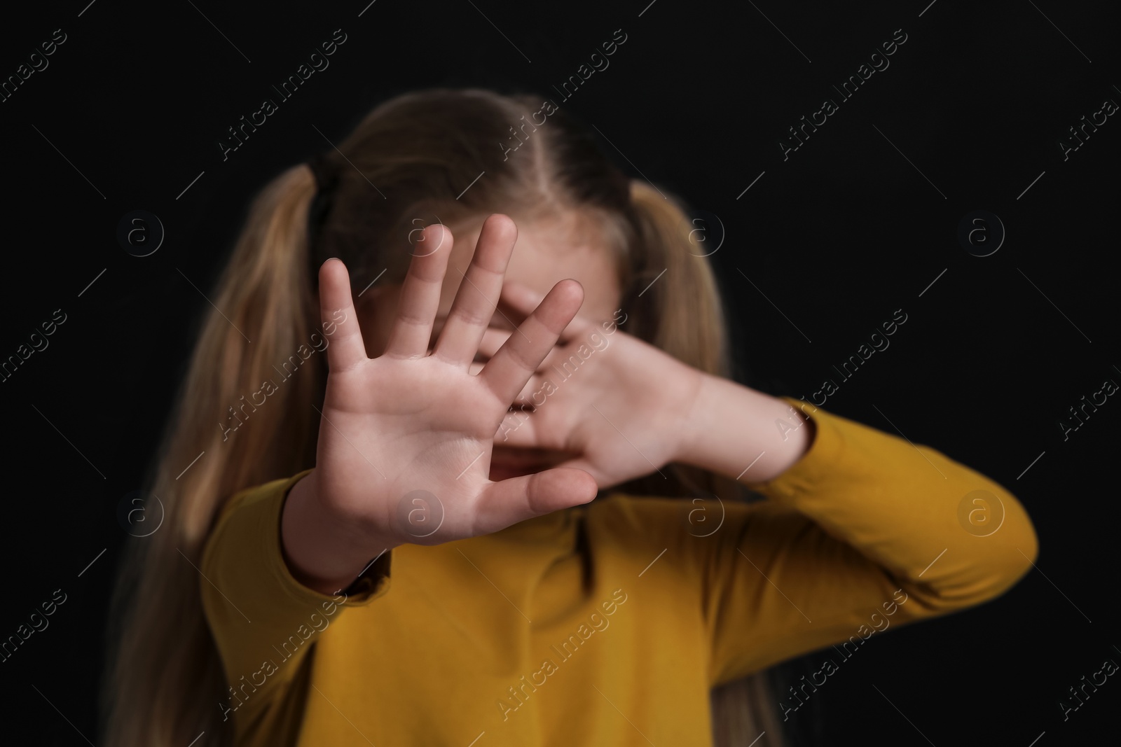 Photo of Girl making stop gesture against black background, focus on hands. Children's bullying