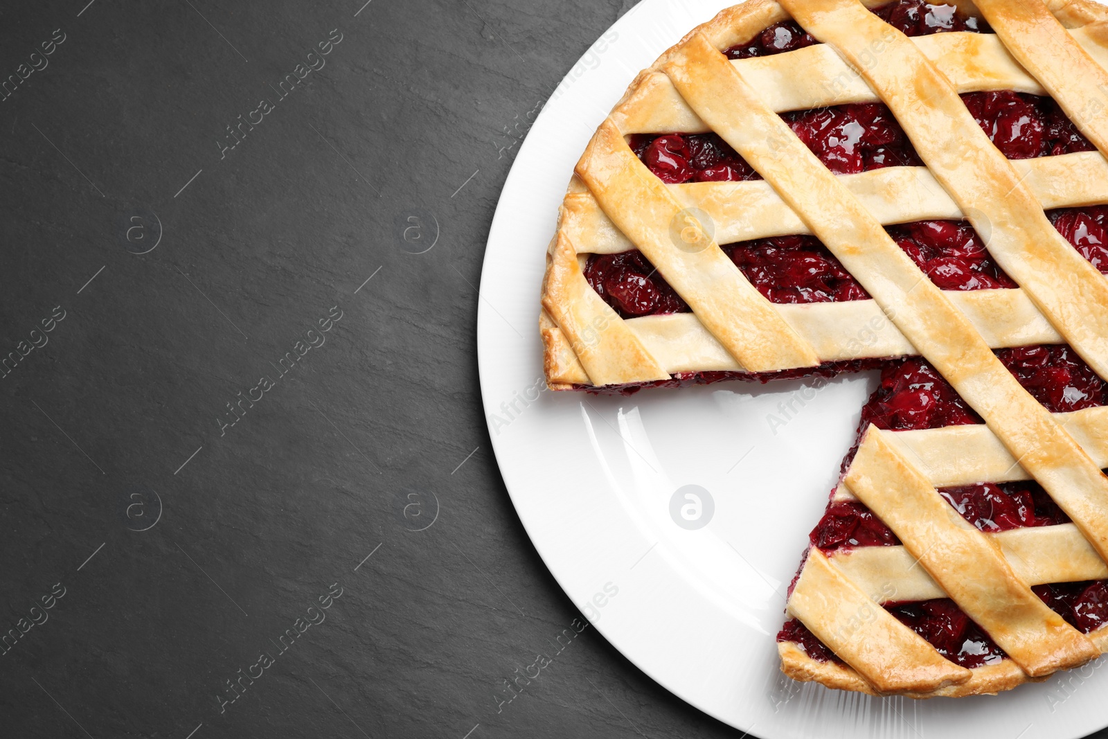 Photo of Delicious fresh cherry pie on black slate table, top view. Space for text