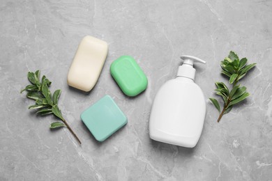 Photo of Different soap bars, dispenser and green plants on light grey table, flat lay