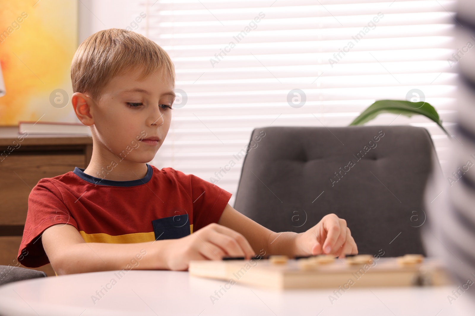 Photo of Cute boy playing checkers at coffee table indoors