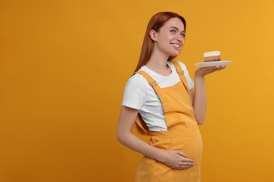 Photo of Pregnant young woman with piece of tasty cake on orange background, space for text