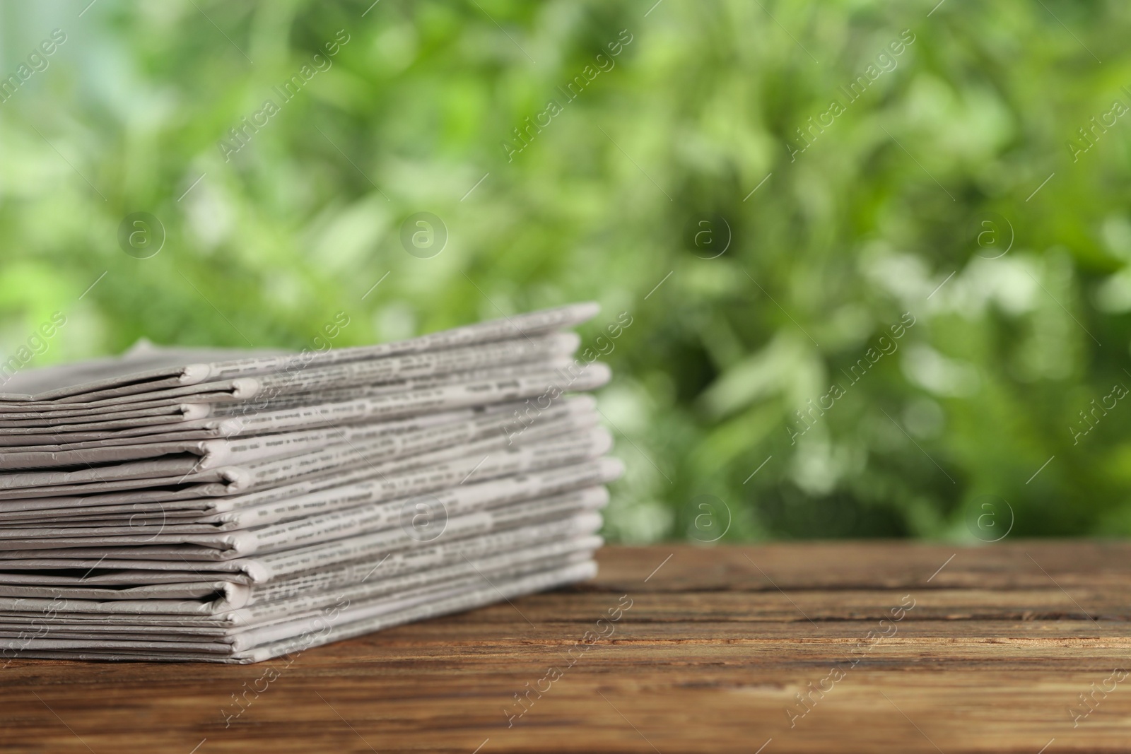 Photo of Stack of newspapers on wooden table against blurred green background, space for text. Journalist's work