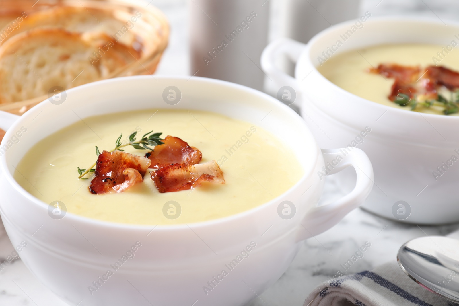 Photo of Tasty potato soup with bacon and rosemary in bowls on white table, closeup