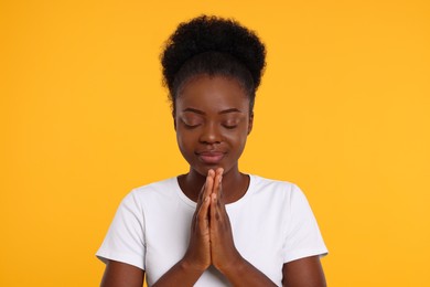 Woman with clasped hands praying to God on orange background