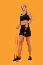 Woman exercising with elastic resistance band on orange background, low angle view