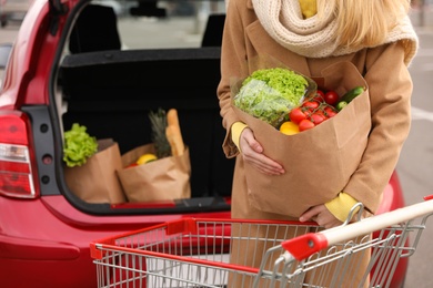 Photo of Young woman with bag of groceries near her car outdoors, closeup