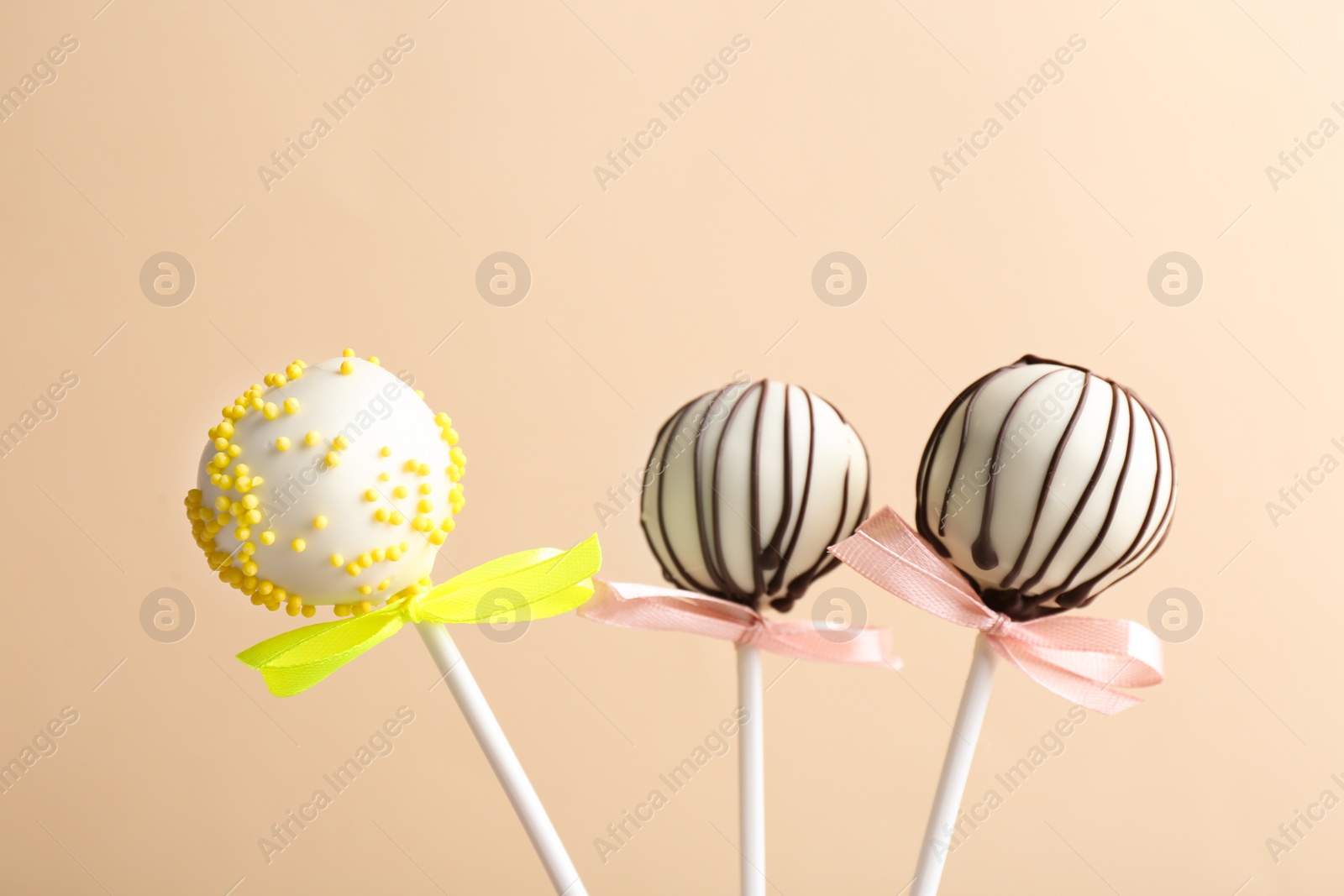 Photo of Tasty cake pops with bows on beige background