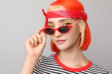 Beautiful young woman with bright dyed hair on light grey background