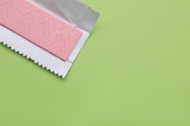 Photo of Unwrapped stick of chewing gum on light green background, top view. Space for text