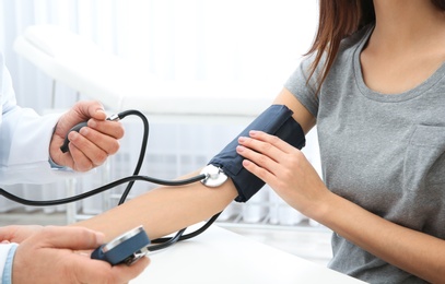 Photo of Young woman visiting doctor in hospital, closeup. Measuring blood pressure and checking pulse