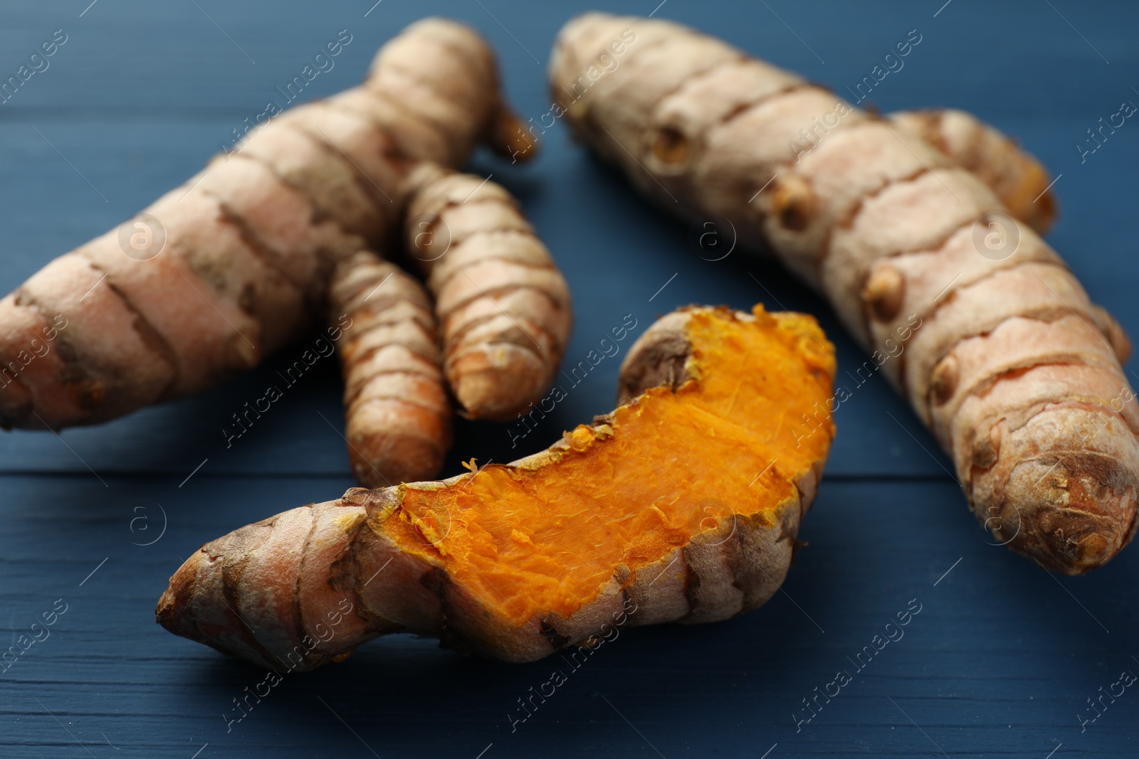 Photo of Raw turmeric roots on blue wooden table, closeup