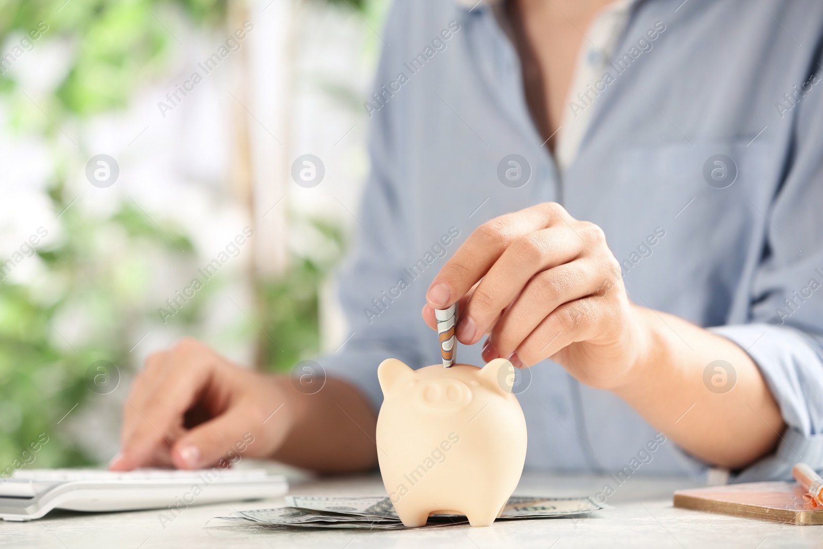 Photo of Woman putting money into piggy bank at table, closeup