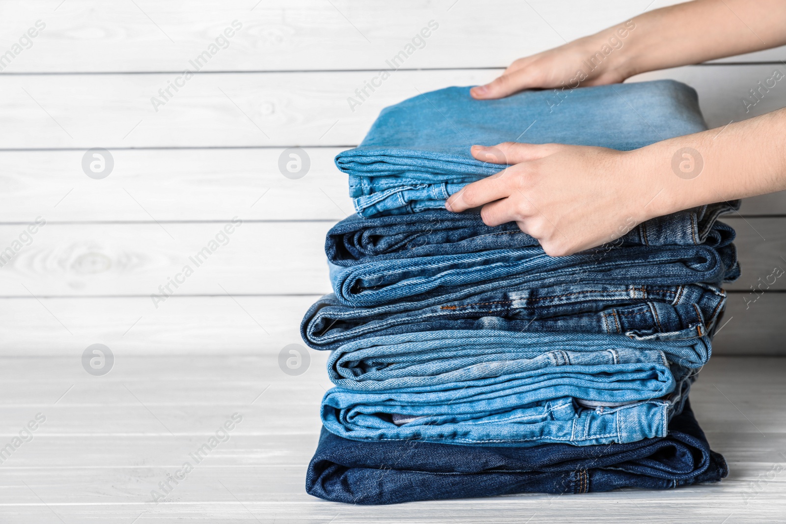 Photo of Woman folding stylish jeans on white wooden table, closeup. Space for text