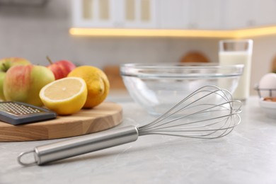 Photo of Metal whisk, bowl, grater and different products on gray marble table in kitchen