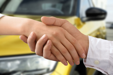 Woman buying car and shaking hands with salesman against blurred auto, closeup