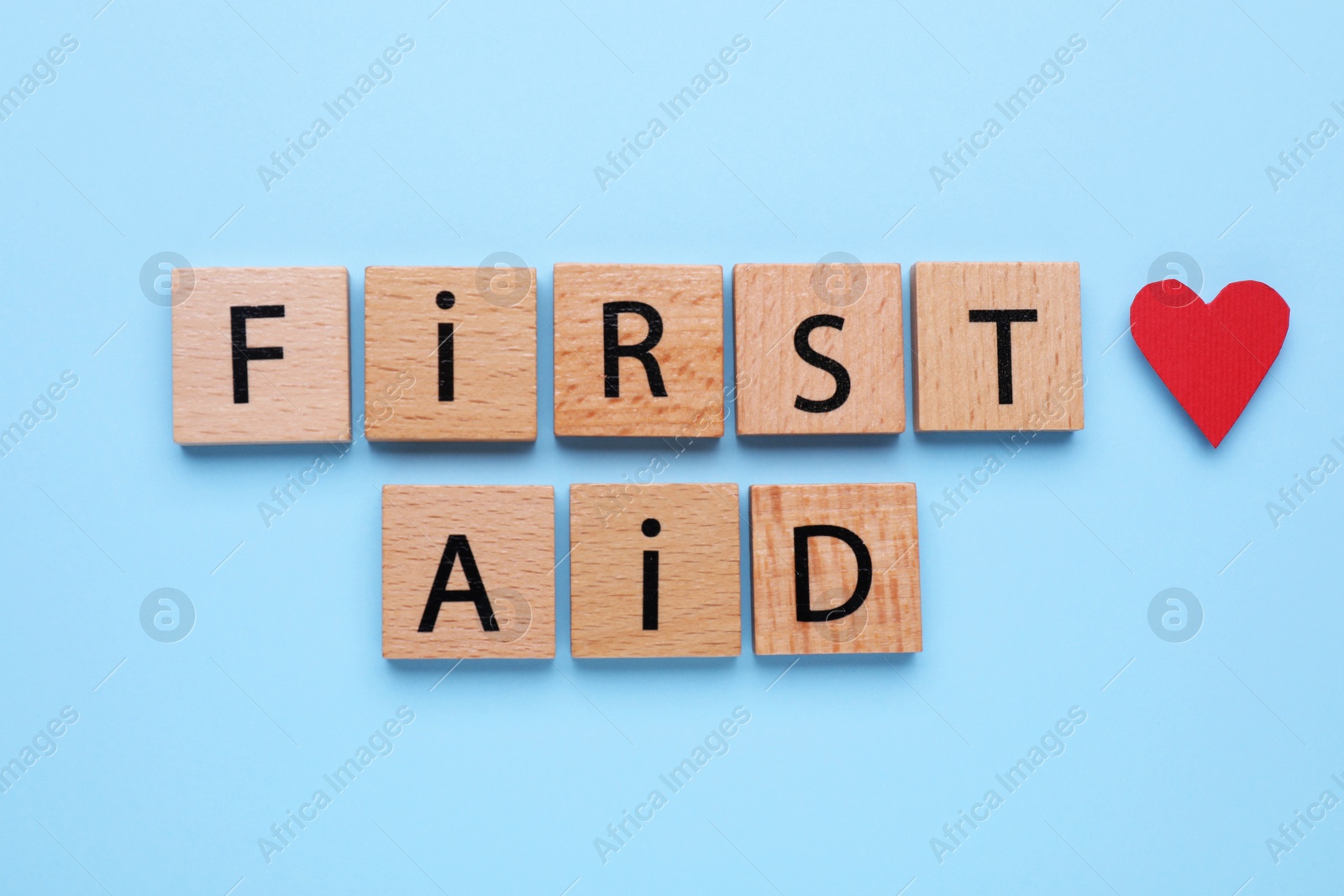 Photo of Words First Aid made of wooden cubes and cardboard heart on light blue background, flat lay