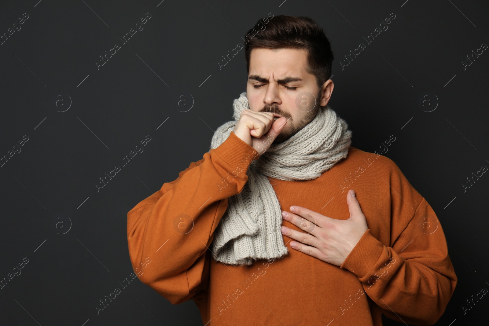 Photo of Handsome young man coughing against dark background