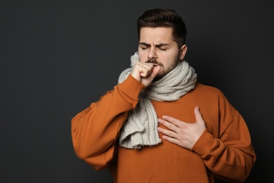 Photo of Handsome young man coughing against dark background