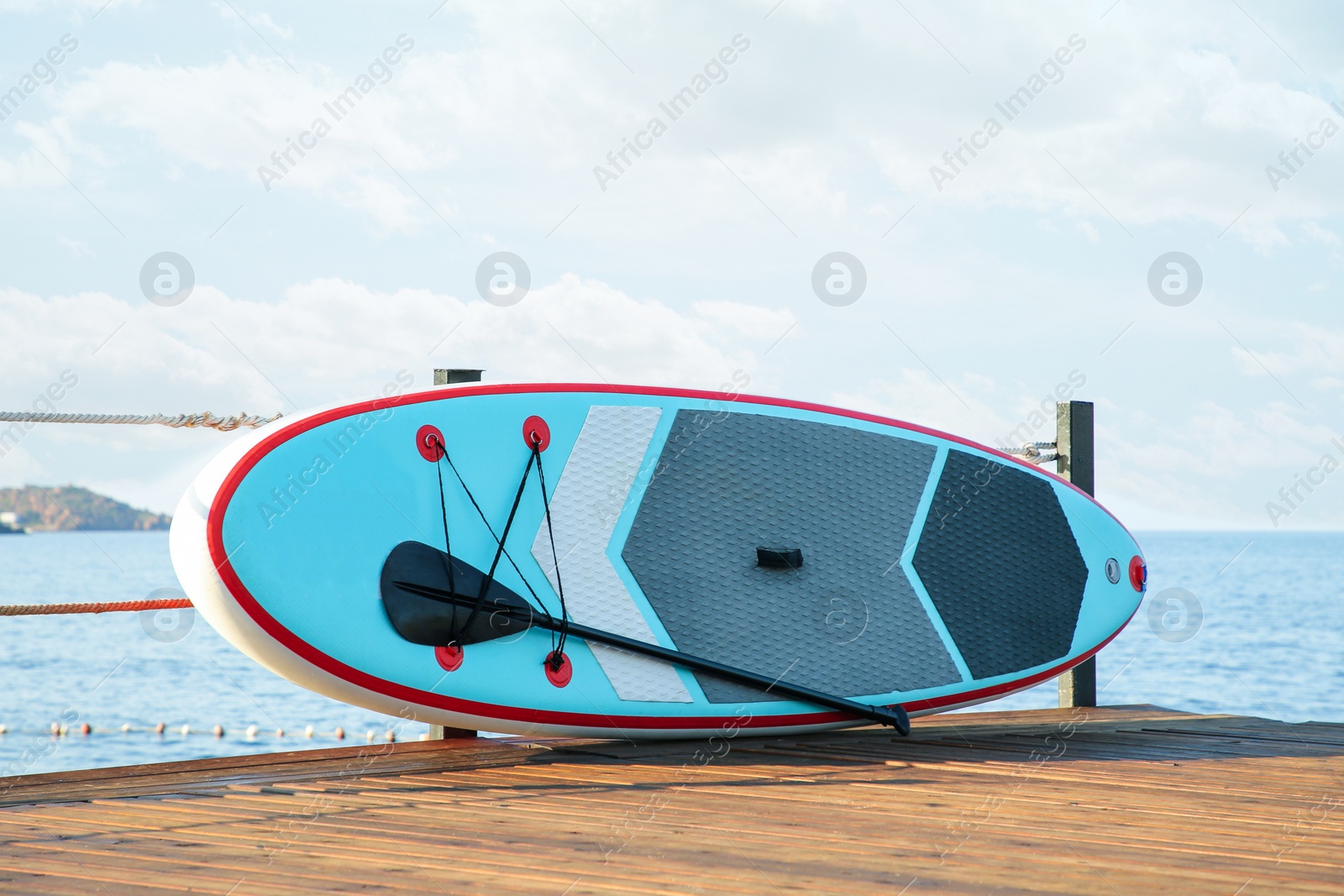 Photo of SUP board with paddle on wooden pier near sea