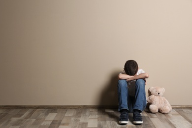 Photo of Upset boy with toy sitting on floor at color wall. Space for text