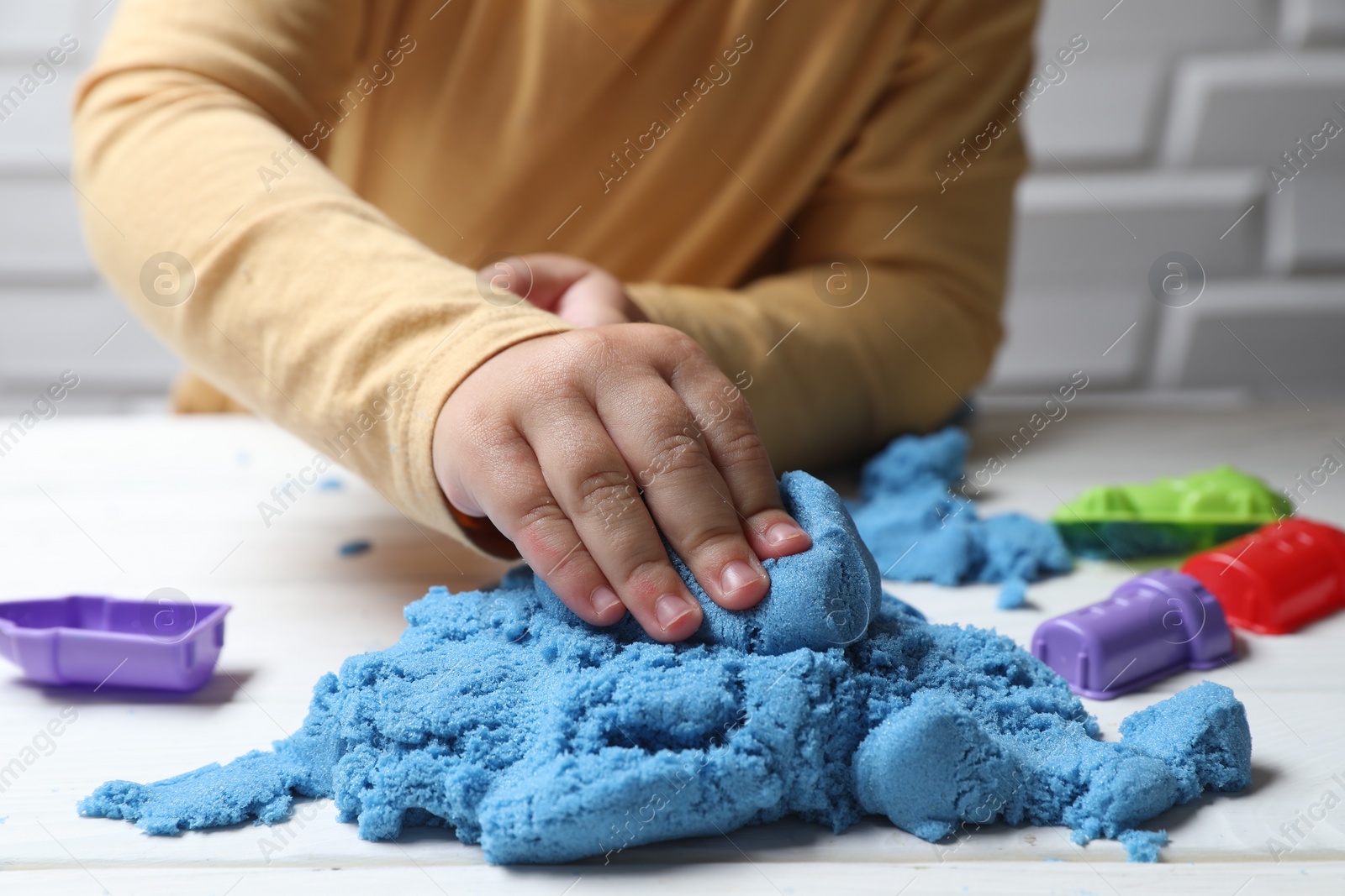 Photo of Little child playing with light blue kinetic sand at white table, closeup