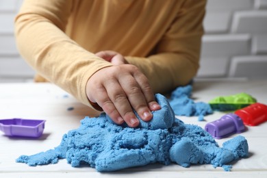 Photo of Little child playing with light blue kinetic sand at white table, closeup