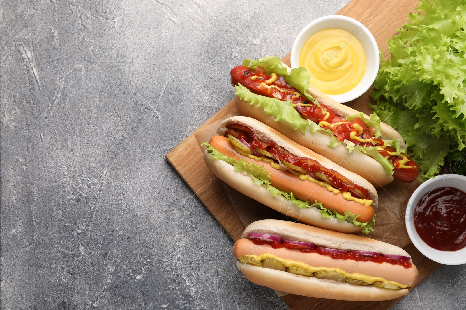 Photo of Delicious hot dogs with different toppings served on grey table, flat lay. Space for text