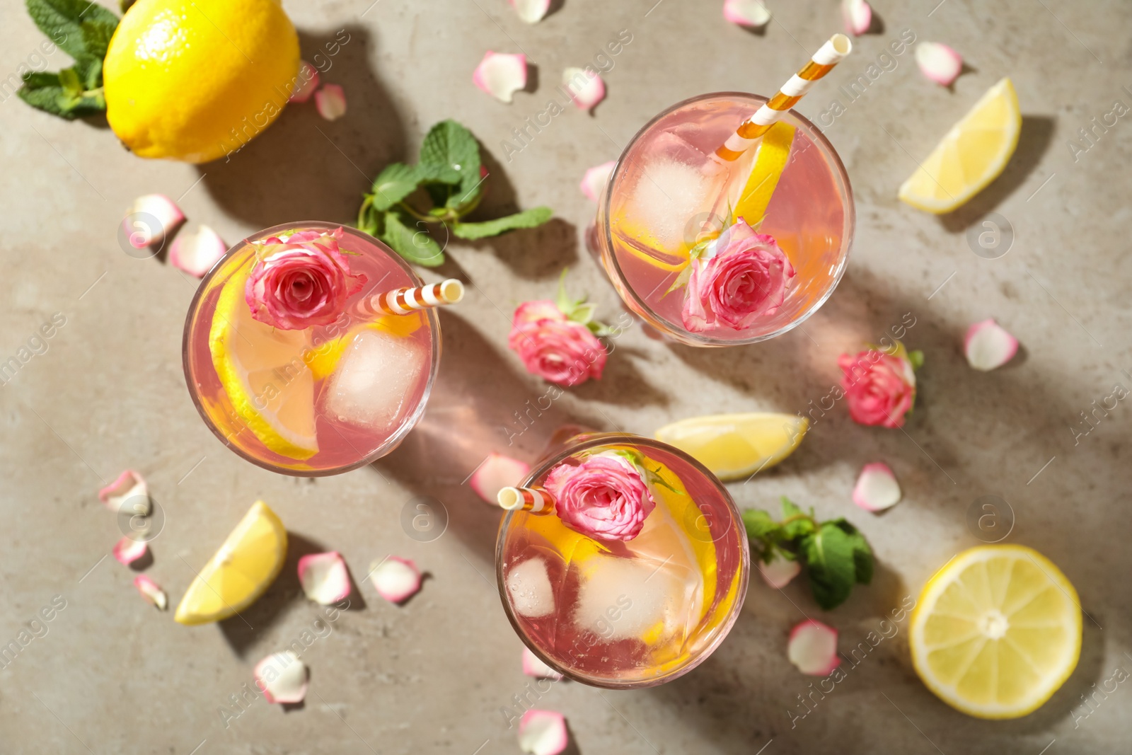 Photo of Delicious refreshing drink with rose flowers and lemon slices on light grey table, flat lay