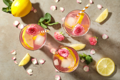 Delicious refreshing drink with rose flowers and lemon slices on light grey table, flat lay