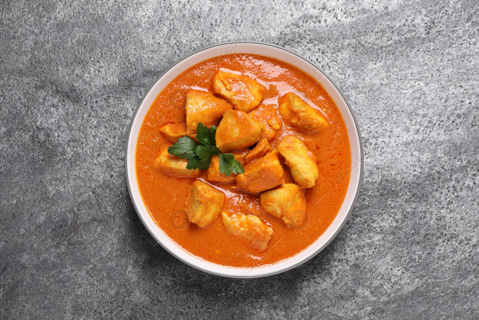 Photo of Bowl of delicious chicken curry on grey table, top view