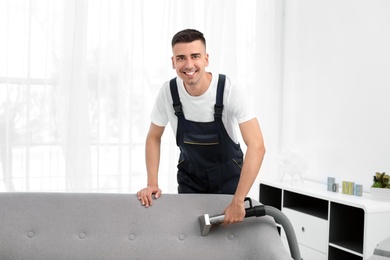 Photo of Dry cleaning worker removing dirt from sofa indoors