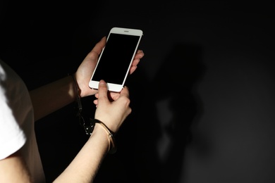 Woman in handcuffs using smartphone on black background, closeup with space for text. Solitude concept