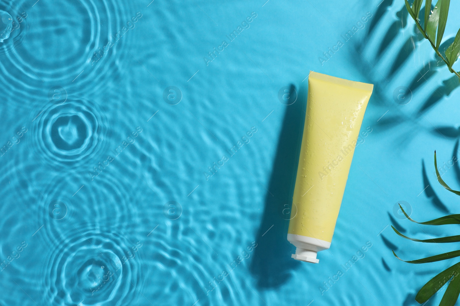 Photo of Tube with moisturizing cream and palm leaves in water on light blue background, top view. Space for text