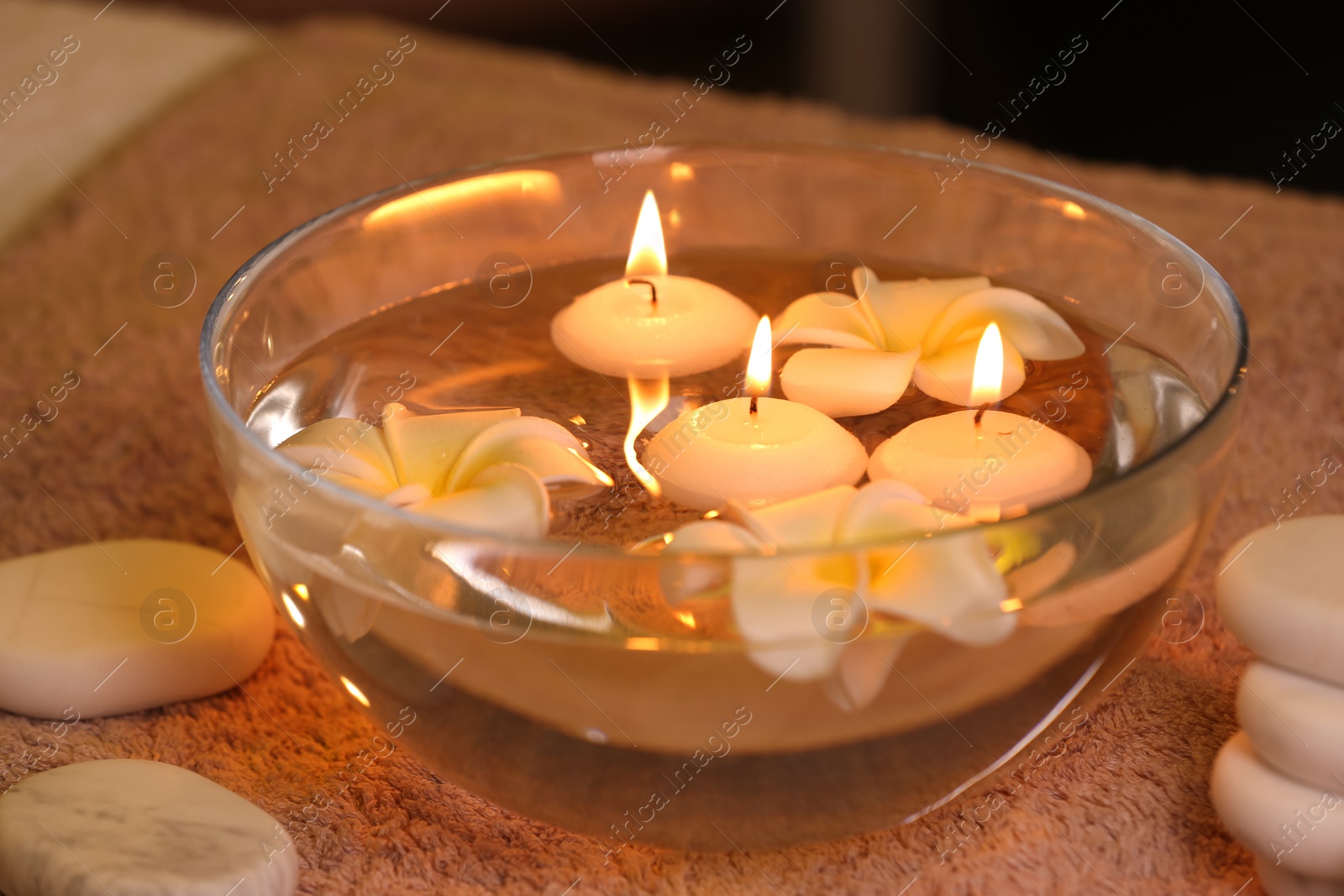 Photo of Bowl with water and burning candles on table in spa salon