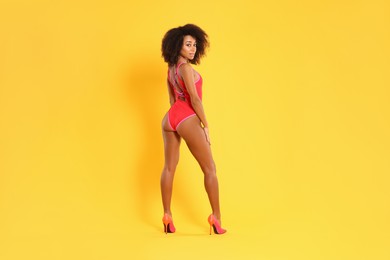 Photo of Beautiful woman in bright one-piece summer swimsuit and stylish high heel shoes on yellow background