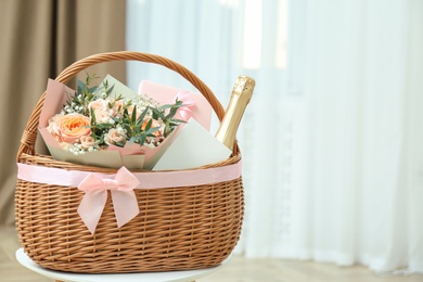 Wicker basket with gifts on table indoors. Space for text
